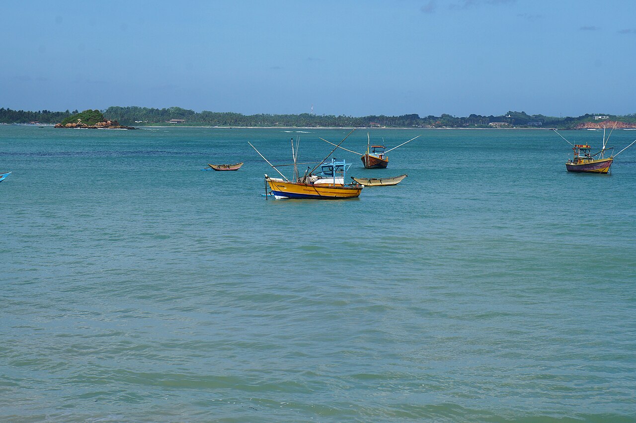 Weligama Bay on Sri Lanka&rsquo;s south coast, a wide sheltered curve of sand with surf lines rolling in and the town behind it